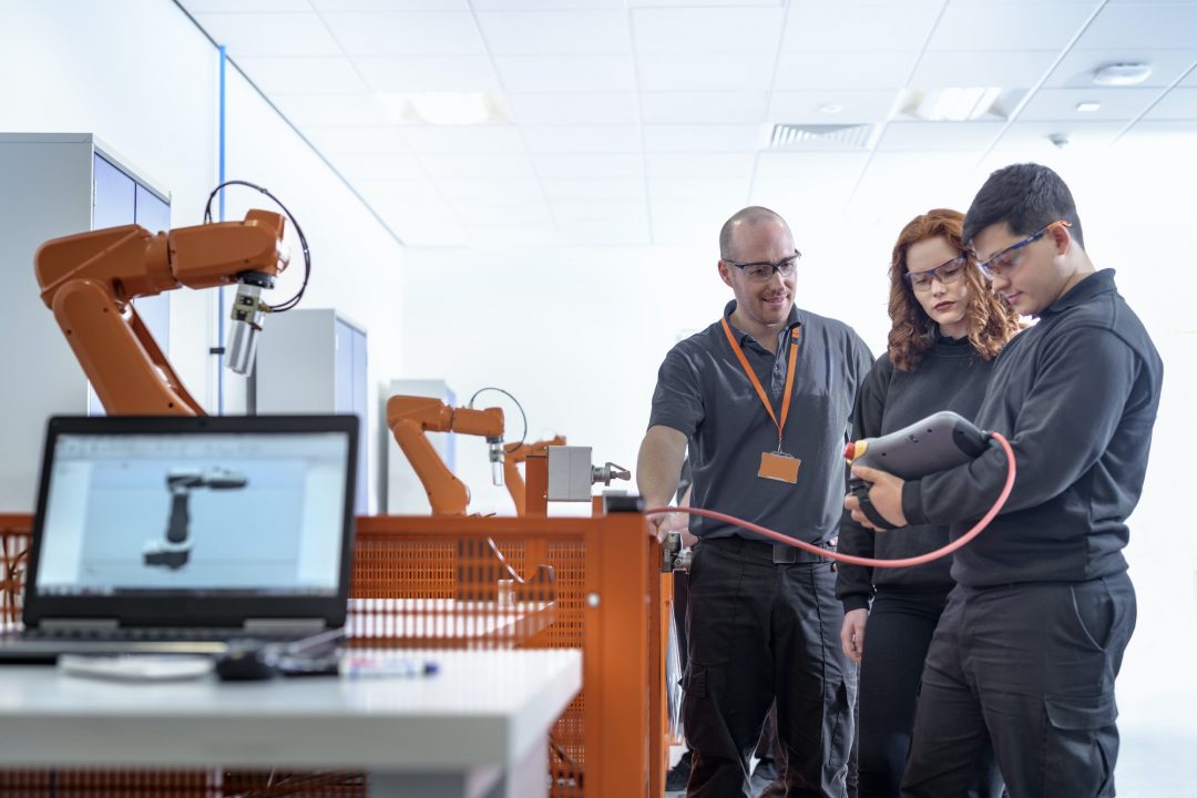 A group of robotics apprentices are using test industrial robots in a robotics facility.